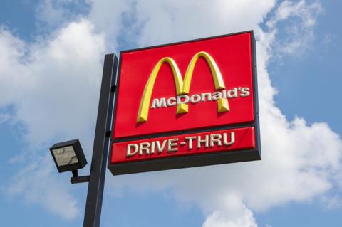 A McDonald's drive-thru sign with blue sky and clouds behind it