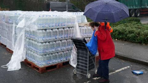 An elderly woman with a shopping cart picking up bottles of water from a water distribution centre