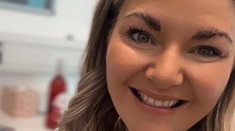 A selfie of Siobhan Gorman who has long wavy blonde hair and is smiling. She is in an office.