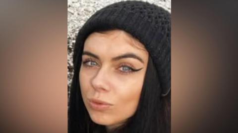Holly Collinson looking at the camera wearing a black woolly hat. She has black hair.