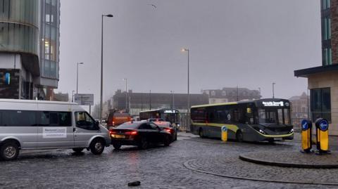 A grey-sky Blackpool town centre junction, congested with a single-decker bus, a grey van and multiple cars