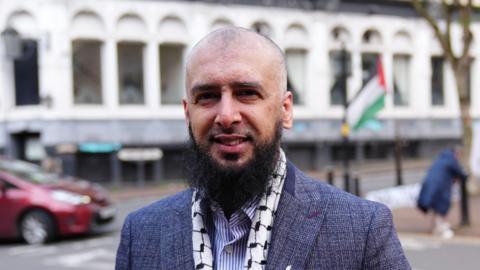 Majid Novsarka wearing a black and white scarf and a blue and white suit