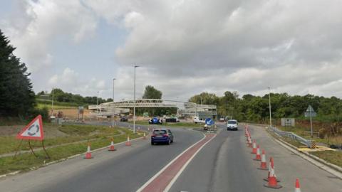  The Landkey Junction on the A361 it shows a roundabout and traffic moving in both directions. The road is lined with traffic cones. 