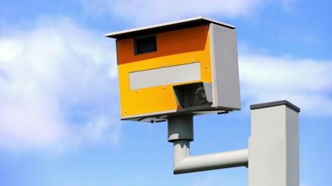 A static speed camera against a blue sky with some clouds