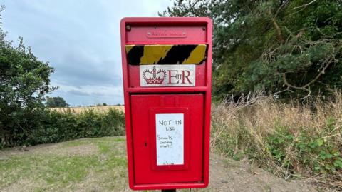 A post box with a sign on it saying 'NOT IN USE - snails eating mail' - with the date of 11 July 2024 on it 