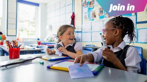 Two girls in a classroom laughing.