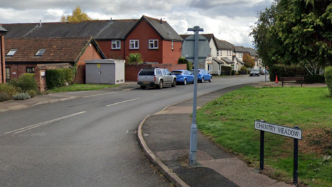 An streetscape with a sign reading Chantry Meadow, there are houses and cars are along one side of the road