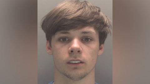 A mugshot of a young white man with hazel eyes and light brown hair. 