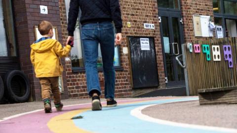 A small boy wearing a yellow raincoat holds his dad's hand as they walk into a polling station in a primary school.