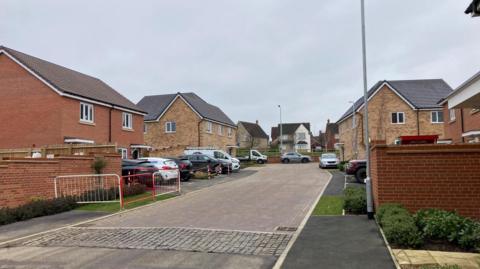 Leveret Gardens with new-build brick homes on both sides of the road. Numerous cars are parked.