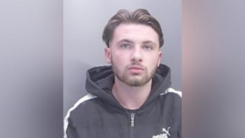 A man wearing a hoody with light hair and a light beard is staring directly at the camera