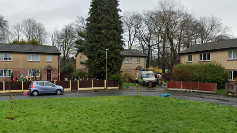 A number of identical brick houses on a cul-de-sac. There is a car parked on the street and a children's toy on the grass in front of another. 