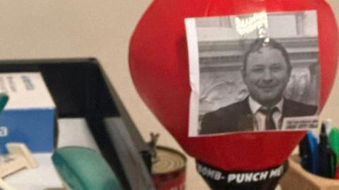 A photo of a punchbag sitting on a desk with the words 'punch me' and a black and white photo of journalist Joe McCann.