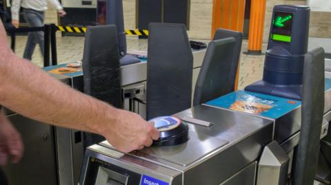 A close up of a man holding an Oyster card to the card reader at the barriers in a London Tube station. 
