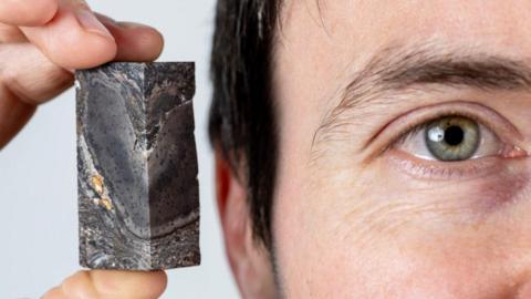A close up image of Dr Sandy Hetherington of National Museusms Scotland and the University of Edinburgh, holding a small sample of the 410-million-year-old fossil 