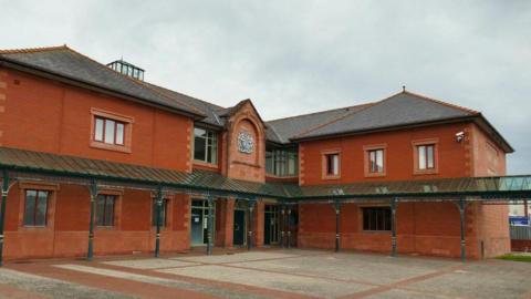 Llandudno Magistrates Court. Red brick building with 12 windows visible. A coat of arms is visible above the door. 