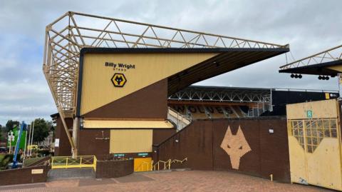 Molineux as seen from the outside. The words Billy Wright Stand are on the side of that stand, which is side on to the camera, while seats in another stand within the stadium are visible in the distance.