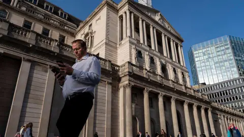 A man checks two smartphones as he walks past the Bank of England