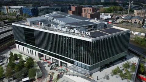Artist's impression of a new building which says University of Bristol on the top. The building has a glass front and a forecourt with trees.