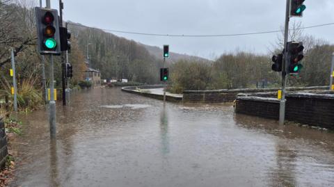 Flooding around a junction between a bridge and a road with traffic lights sticking out of the water.