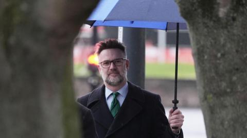 An image of TV auctioneer Charles Hanson wearing a black coat whilst holding an umbrella 