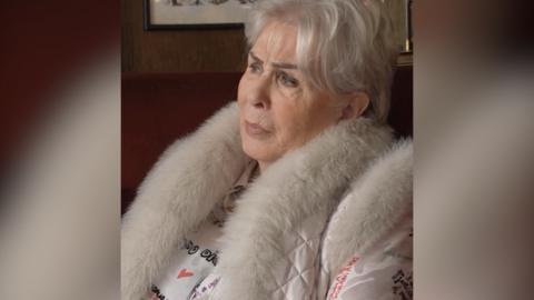 A woman with short white hair wearing a jacket with a white fur collar