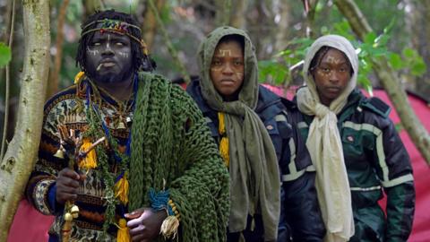 The three members of the self-proclaimed Kingdom of Kubala, clothed in knitwear, standing in woodland following their first official eviction.