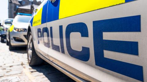 A close-up stock image of a number of police cars parked up on a street. 