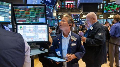 Dealers on New York Stock Exchange on 6 November 2024. A man with a pen in his hand and a notebook is looking up at a computer screen showing prices