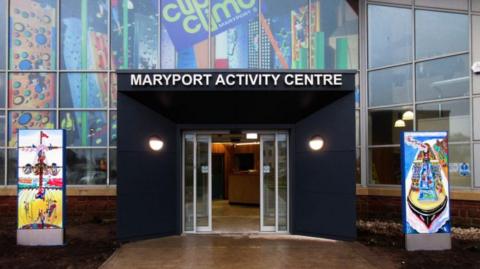 The entrance to Maryport Activity Centre has black panels and lights surrounding the automatic door. The building has glass panelled walls.