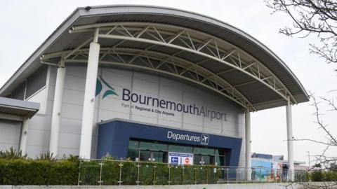 Bournemouth Airport Departure building - a grey building with a large portico held up by a number of columns and a blue surrounding  to the glass entrance and a green hedge at the front.   
