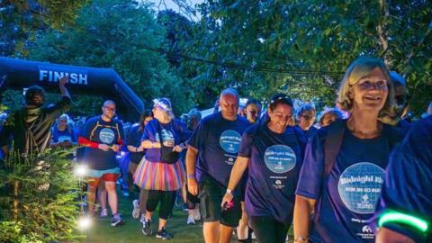 A group of people in matching fundraising t-shirts walk under an inflatable arch with the word finish across the top.