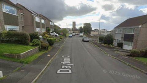A street view of Dayton Close in Crownhill, Plymouth. The road is at the centre with grey and brown houses either side