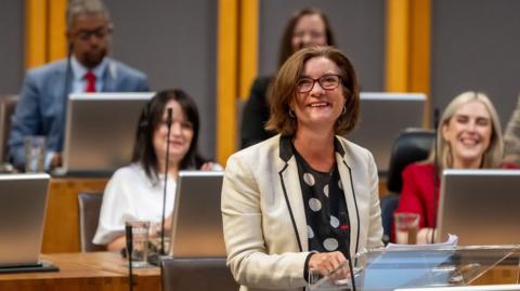 Eluned Morgan, wearing a white suit, smiling in the Senedd