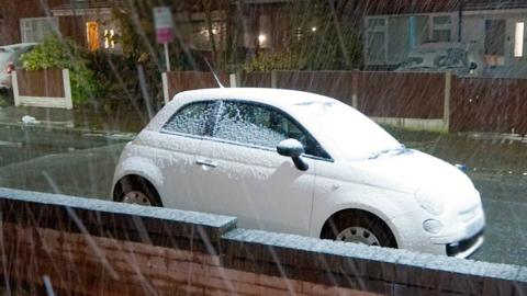 A white car covered in snow on a suburban street