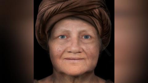 The early reconstruction of the face of The Kendal Woman. She is a middle-aged woman wearing a dark turban and she has blue eyes.