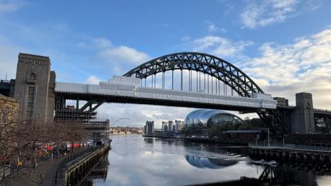 The Tyne Bridge. Large white sheets cover much of the bridge where repair work is being carried out. Scaffolding can be seen underneath the bridge by the concrete towers.