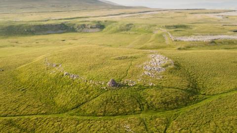 General view with Yorkshire Dales National Park surrounding the stone monument. The monument is in the centre of the image - the prominent conical cairn structure nearer the bottom is more modern and not part of the scheduling.