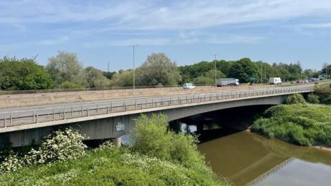 A view of the Over Bridge over the river Severn with light traffic on it. Underneath the water of the river, which is dark brown, can be seen flowing