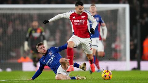 Ipswich Town's Leif Davis and Arsenal's Gabriel Martinelli battle for the ball during a Premier League match. Davis is wearing Ipswich's blue and white strip, while Martinelli is wearing Arsenal's red and white kit. 