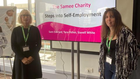 Sam and her colleague stand in front of a TV screen during a presentation. It reads: 'The Samee Charity: Steps into Self-Employment'.