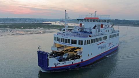A drone view of a Wightlink car ferry with mud flats and the masts of a yacht marina seen in the background