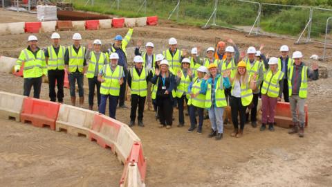 A group of people in high hats and visible jackets standing on a building site.