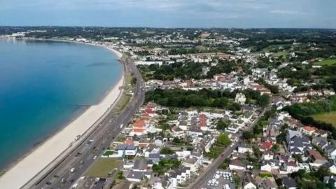 A coastal community with houses and a coast road with a beach and sea beyond.