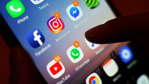 A generic image of a phone and someone about to tap on an app. There are notifications on a number of apps, indicating messages.