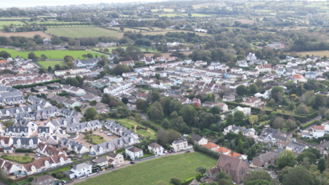 A drone image taken of above Jersey. There is a number of green space and large fields. There is a number of houses in the image too.