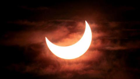 The sun being covered by the moon. There are clouds beside it that are glowing red because of the light.