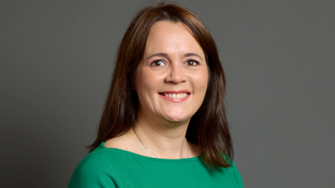 Woman with brown hair and a green dress smiles for official portrait 