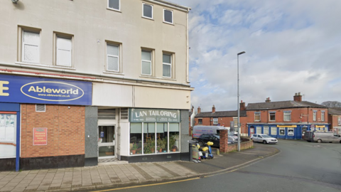 A street with a shop with a blue sign reading Ableworld in yellow writing