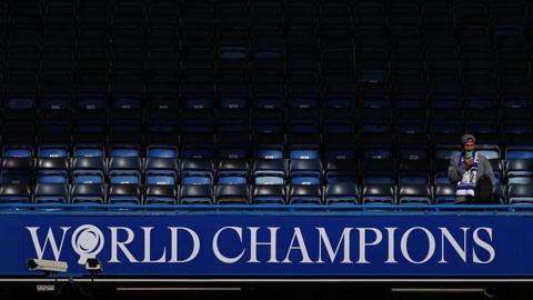 A lone supporter of Chelsea FC sits in the stands above “World Champions” signage inside Stamford Bridge 